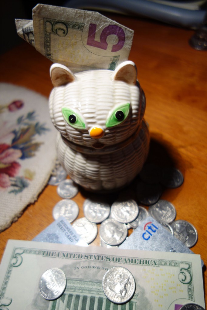 Cat piggy bank with bills, credit cards and coins over flowing.