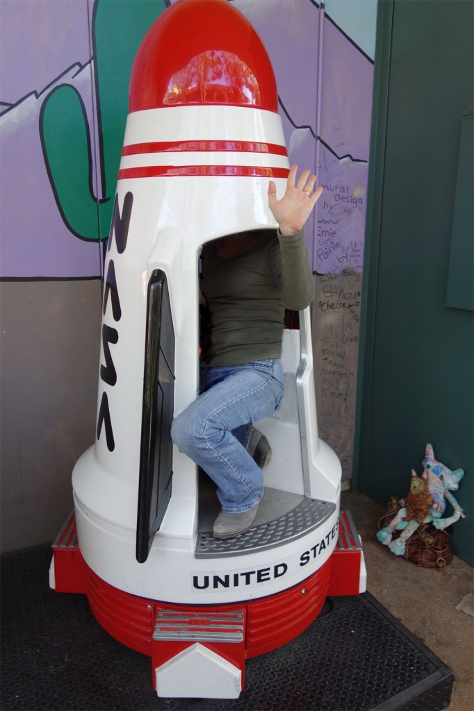 Crazy Cat Lady tries to fit inside a childs spaceship at an arcade.