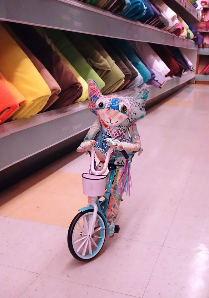 The Chairman peddles his bicycle down an aisle of Joanns Fabric store.