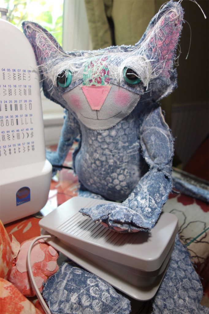 Deni, the denim cat doll, controls the foot pedal for the sewing machine.