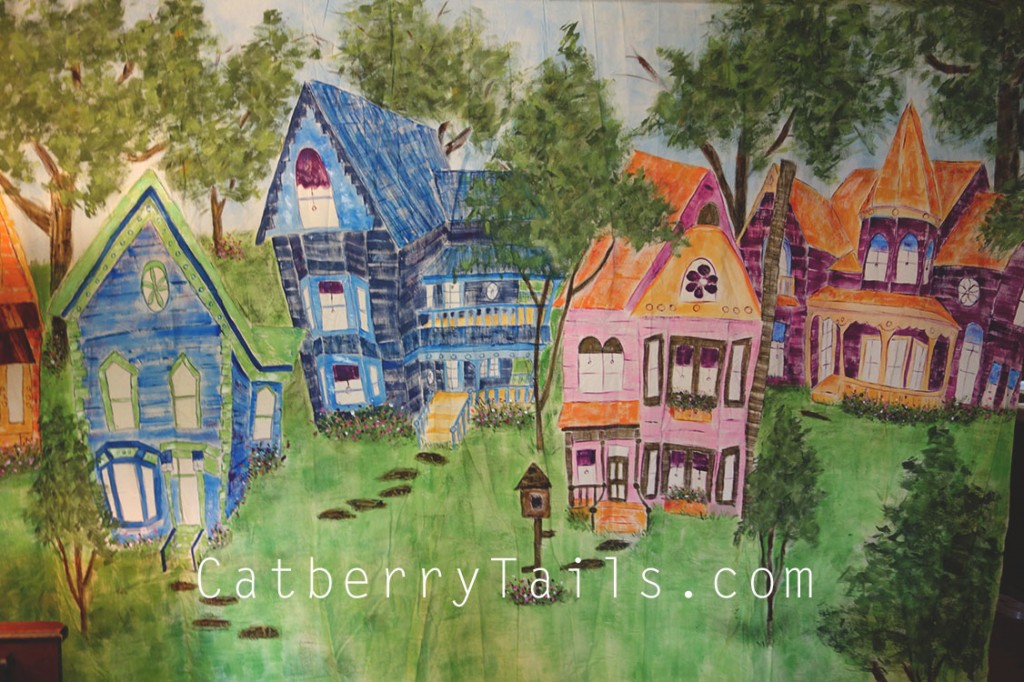 Colorful, huge hand painted canvas of whimsical houses surrounded by trees and grass and birdhouses.
