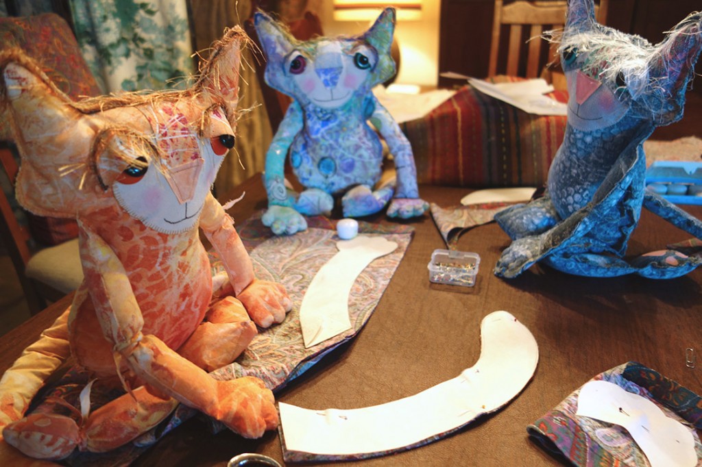 Three of the whimsical cat dolls are cuting out curved tail pattern pieces.