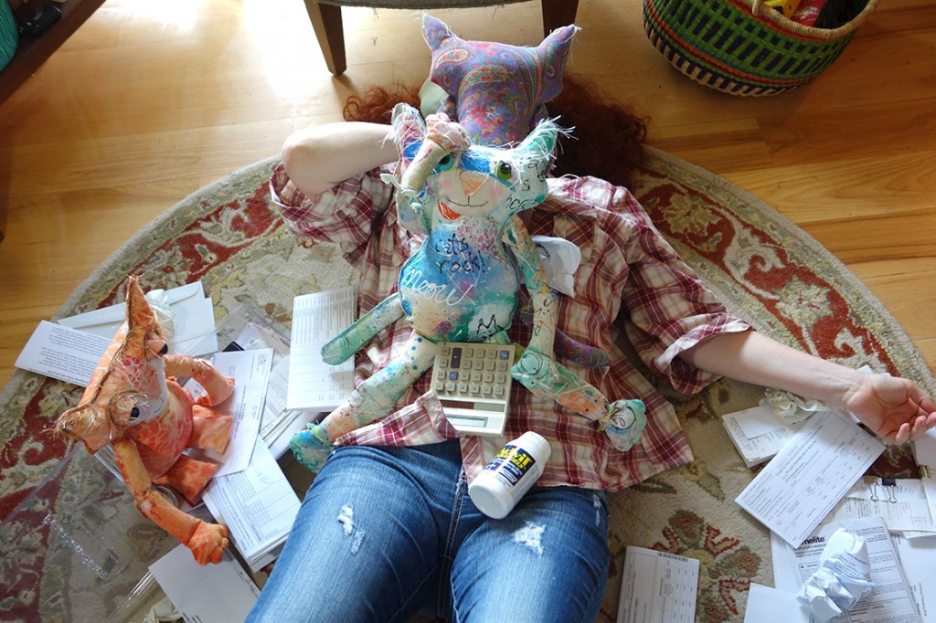 The Kreatrix flat out on her back surrounded by papers, a calculator, a bottle of Advil and the cat doll community.
