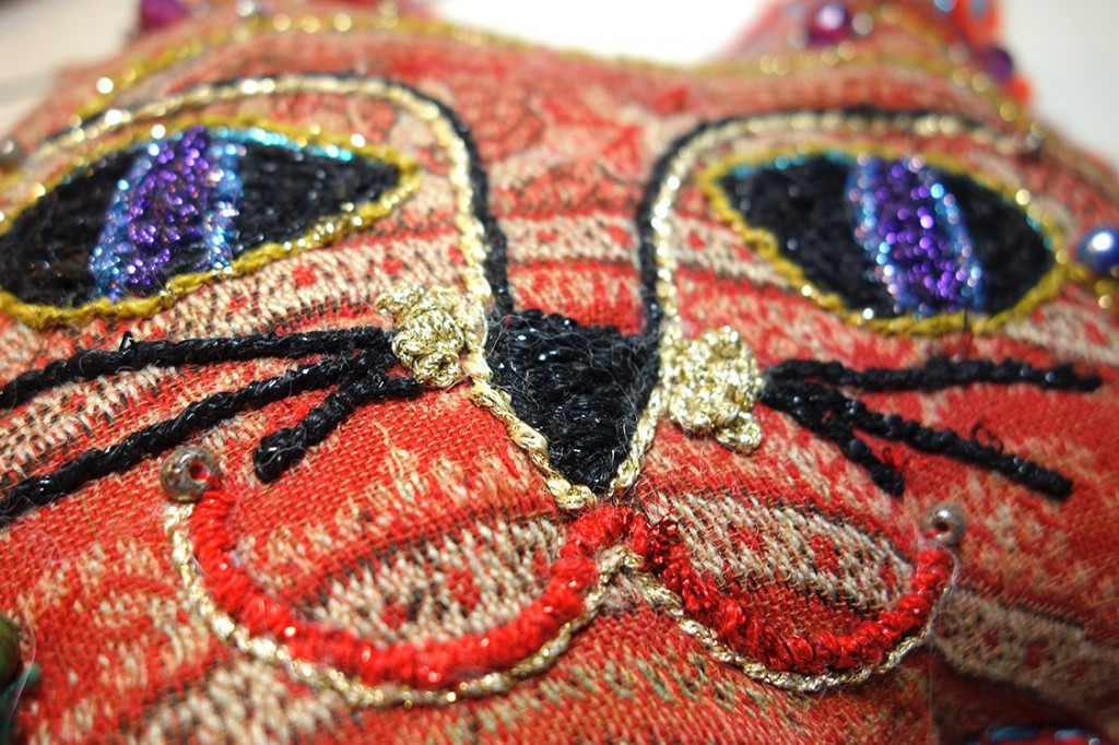 Closeup of the the embroidered cat dolls face. Very colorful and sparkly.