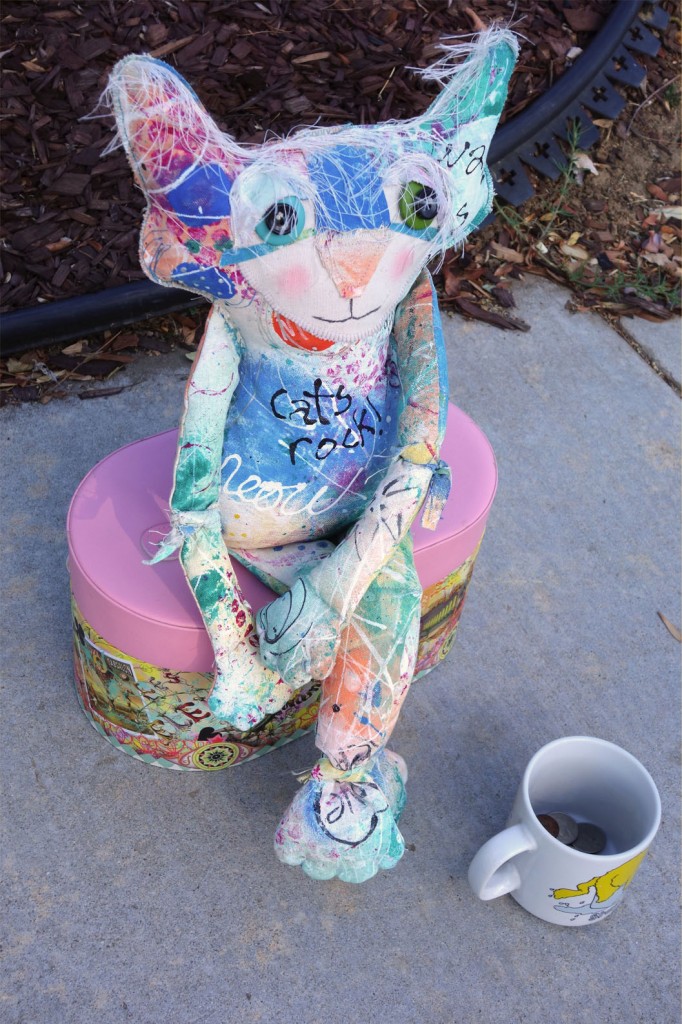 Chairman sits on his suitcase at the sidewalk. A coffee cup with coins in it sits in front of him.