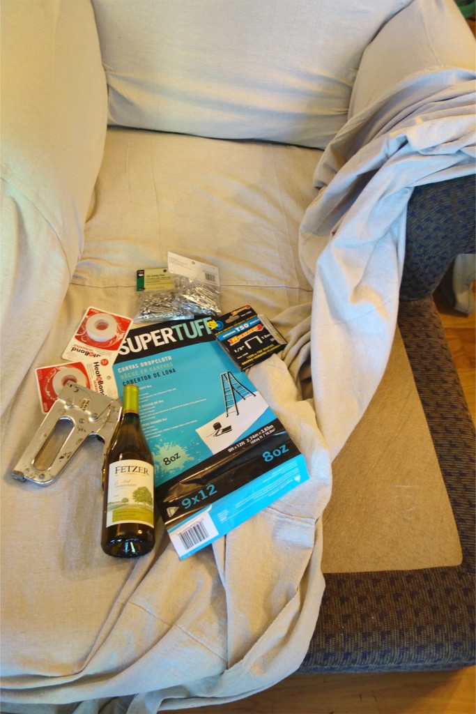 Photo of supplies used for the project laying on this huge chaise. Supplies include a staple gun, safety pins, a large drop cloth and a wine bottle. Yes. Wine bottle.