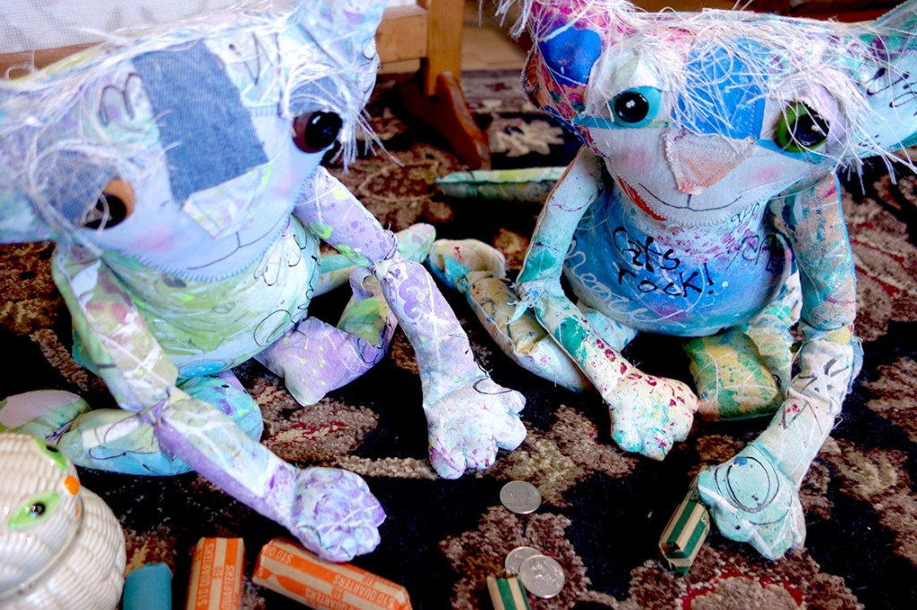 Two adorable cat dolls counting coins on the floor with the curse jar nearby.