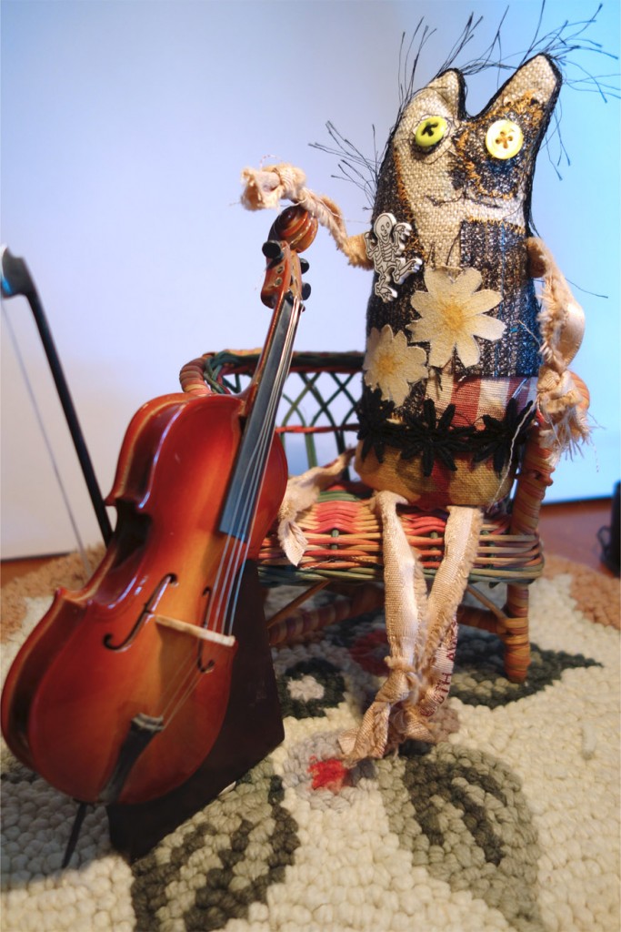Frankencat poses with his cello as it rests on the cello stand. Very professional musician type photo.