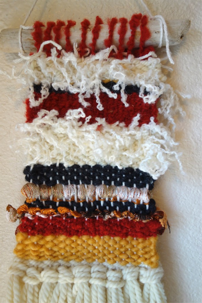 A woven wall hanging with colorful and fun types of yarn.