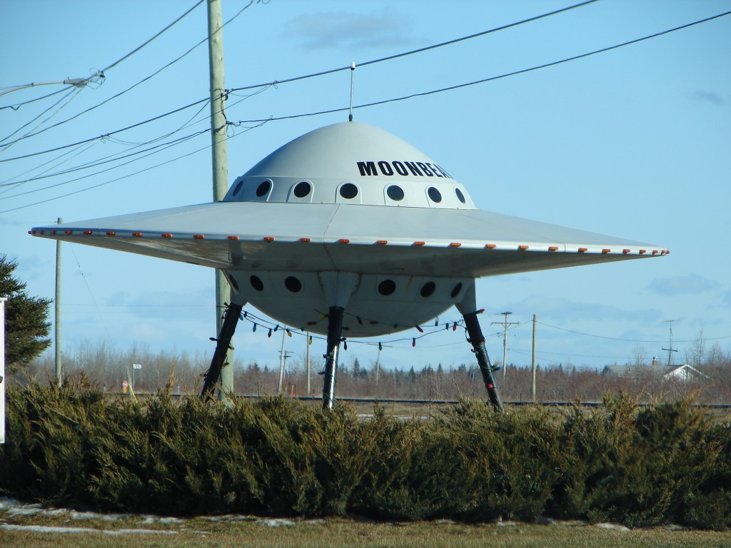 Photo of a very stereotypical flying saucer parked in a field of grass.