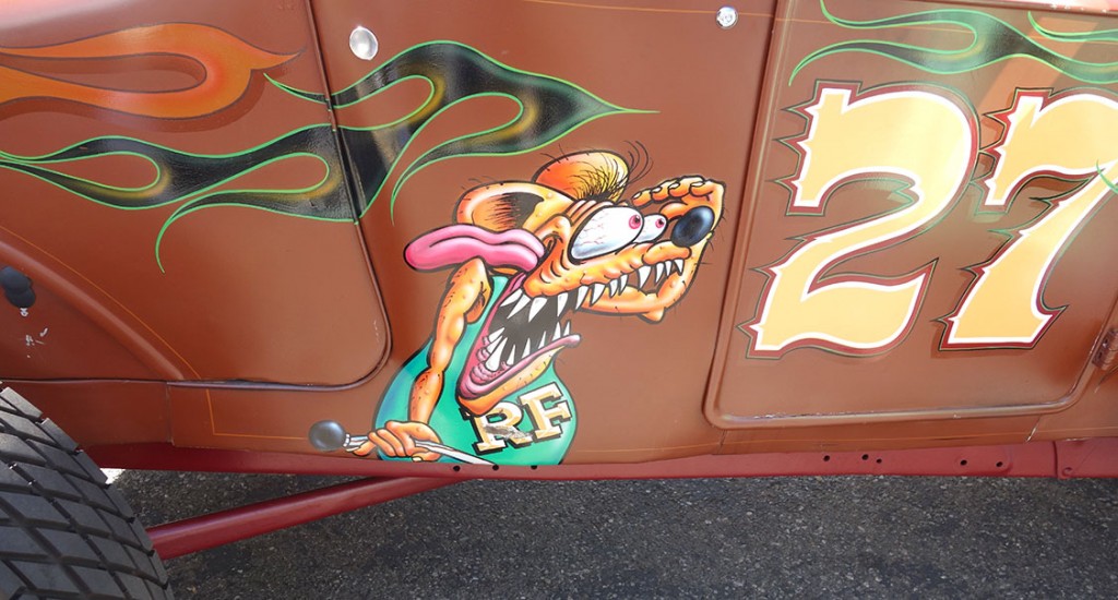 Hysterical cartoon drawing of Rat Frink emblazoned on the side of a hot rod. Rat fink has big teeth and bulging eyes.