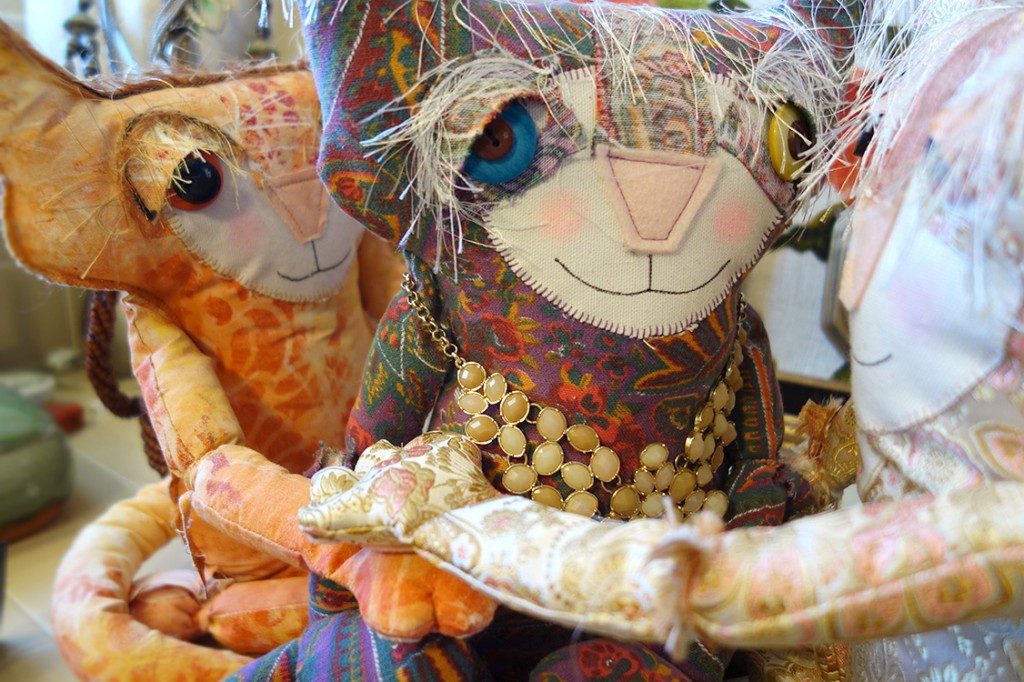 Three soft sculpture cat dolls and in a group embrace.