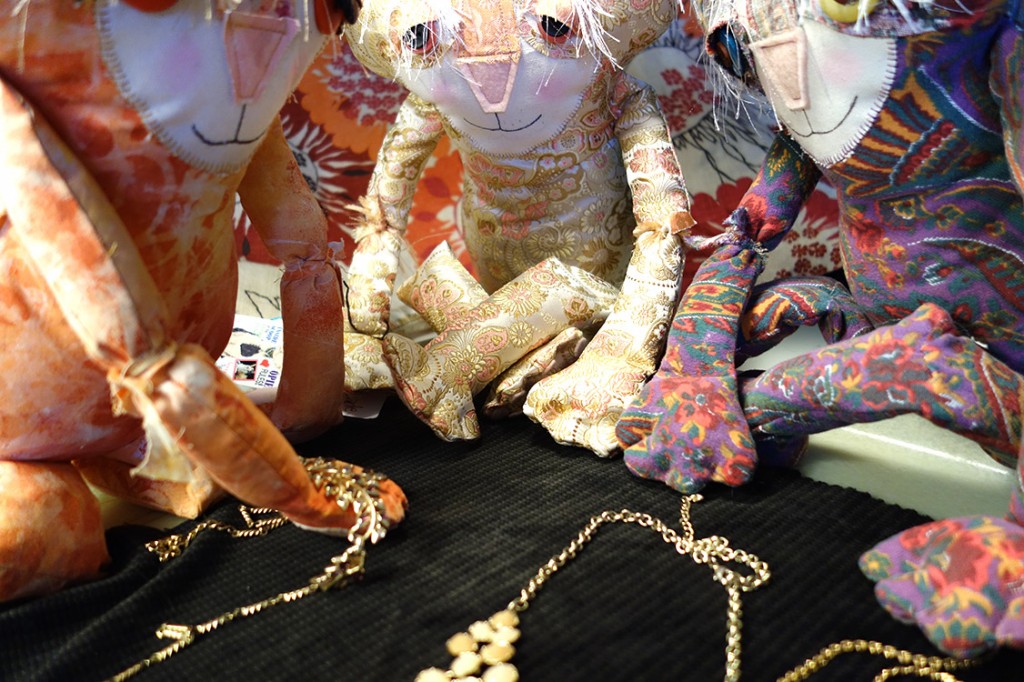 Three adorable soft sculpture cat dolls are huddled around the jewelry. Ginger is holding one across her paw.