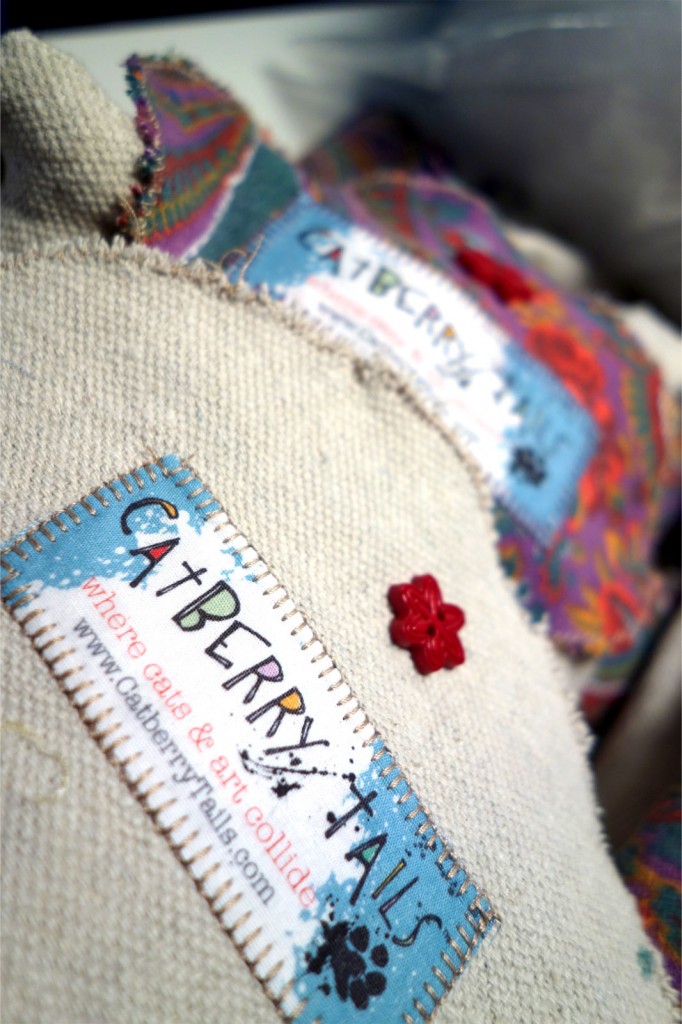A photo of the Catberry Tails label sewn onto fabric and a button flower above it.