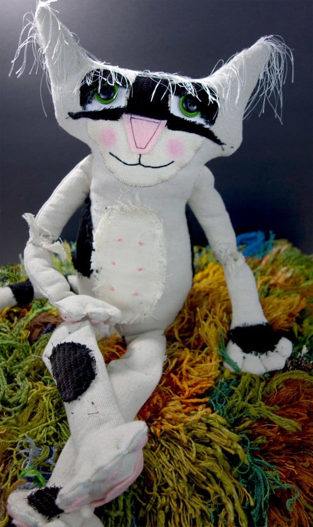 Bandit, an adorable black and white soft sculptured cat doll sits on one of the shag rugs looking quite pleased with himself.