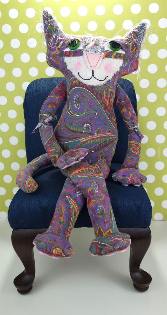 Penny, the adorable soft sculptured cat doll, sits with her legs crossed on a navy blue doll chair.