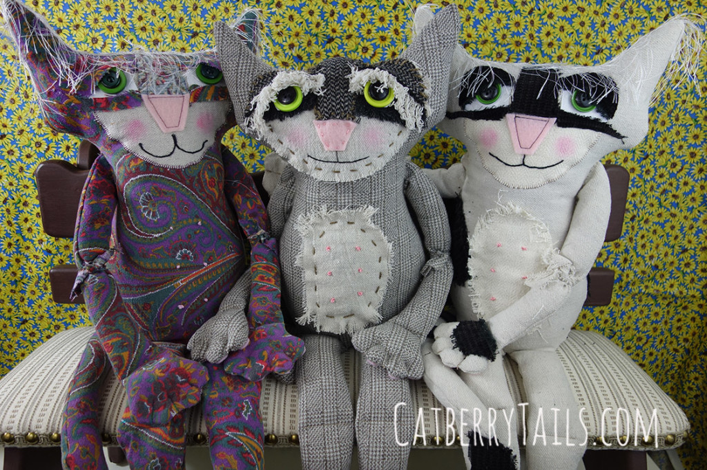 Rascal is seated with two other recently sewn cat dolls, one of whom is a female and is holding hands with him.