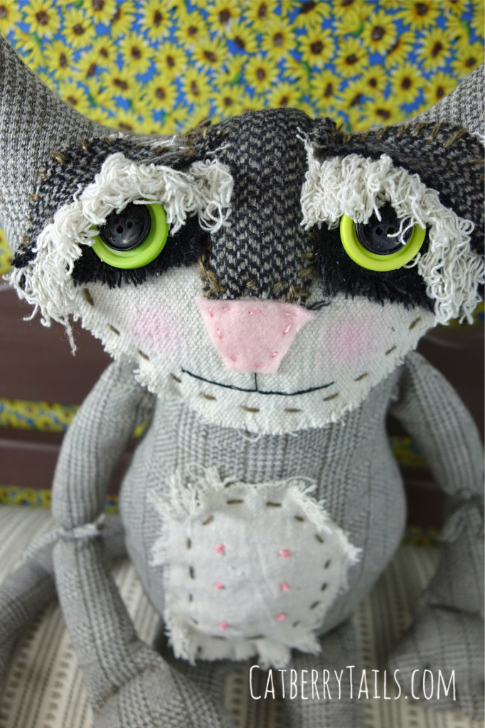 Up close photo of Rascal's face. His eyes are beautifully fringed with textured black, frayed wool and ivory yarn.