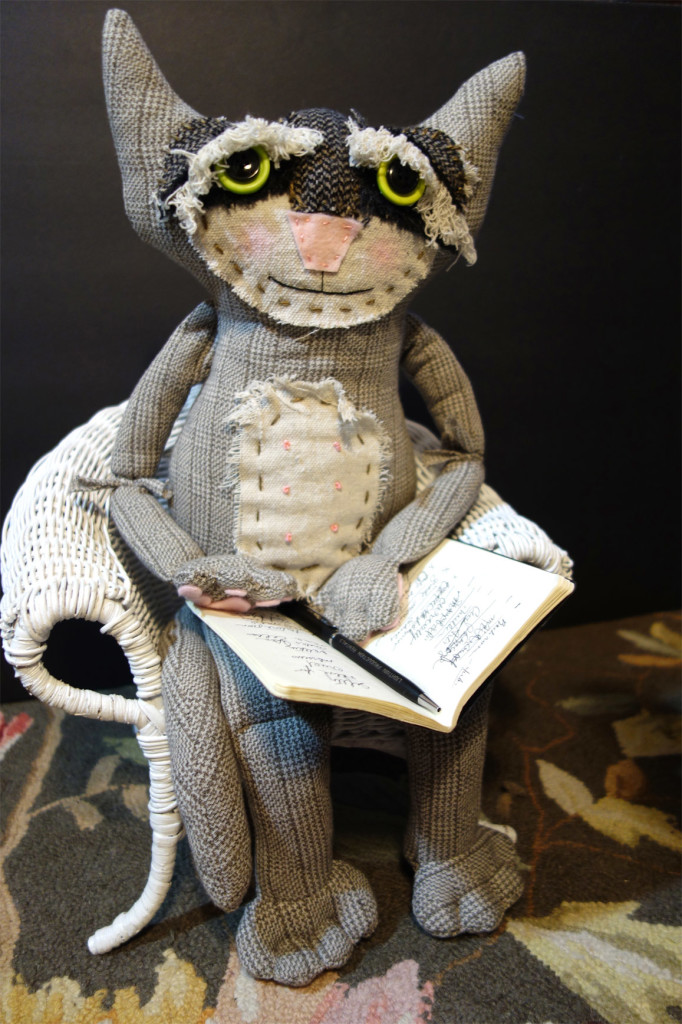 Very cute soft sculpture cat doll named Rascal sits in a chair with a pad and pen just like a shrink would do when treating a patient.