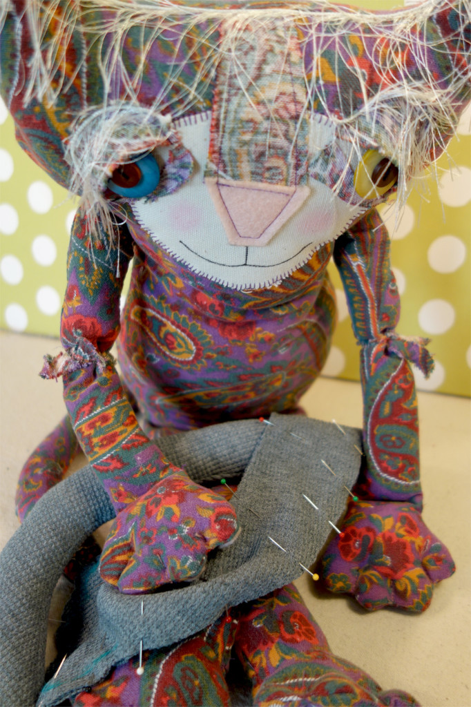 Eve, the cute soft sculpture cat doll made out of sixties paisley fabric is doing some hand sewing on a new doll.