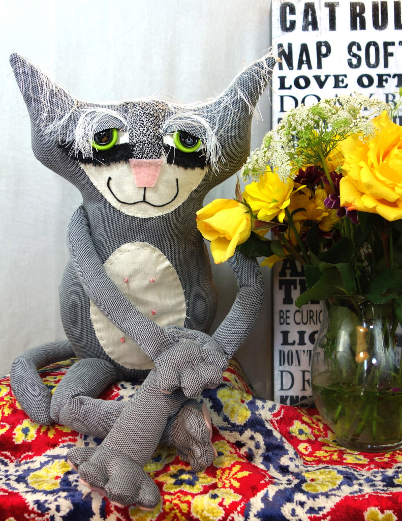 A soft sculpture cat made from upcycled clothing. He is grey and has an adorable ivory belly patch. 
