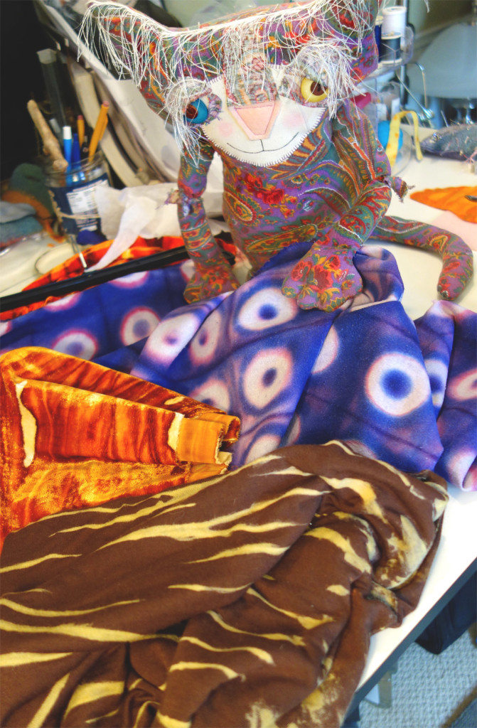 Soft Sculptured Cat doll posing with an array of hand-dyed fabric.