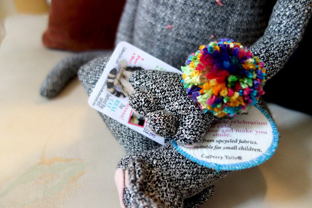 A fluffy colorful pom-pom is attached to the paw of a soft sculptured cat.