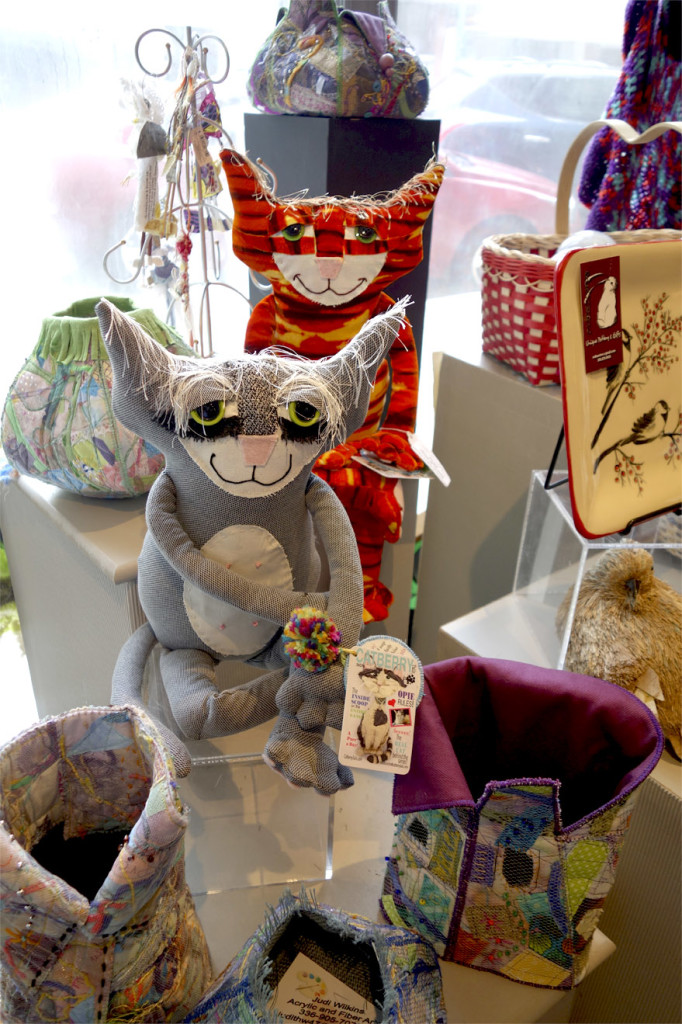 Two soft sculptured cats pose proudly in a gift shop of a gallery.