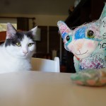 Wally the real cat and a cat doll sit at table.